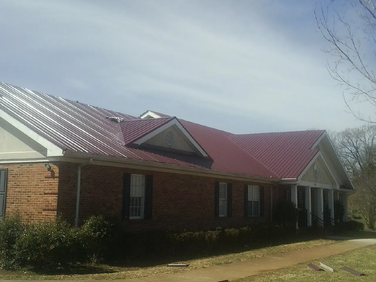 Red metal roof with gabled entries on a long brick building, from a Hail Damage Roof Repair job in Yukon