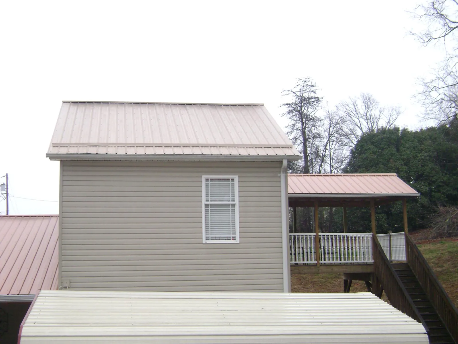 Tan metal roofs on a two story addition and attached porch, from a Roof Replacement job in Yukon